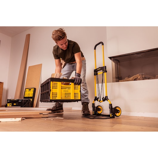 Photo of STANLEY STST98022L folding hand truck and yellow-black storage crate in indoor workspace.