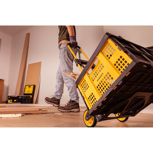 STANLEY STST98022L yellow and black utility cart being pulled in a workshop, side angle.