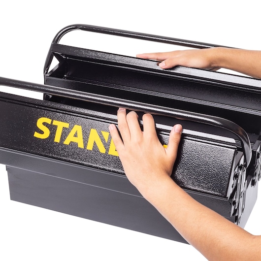STANLEY STST98724LA black metal toolbox being opened by two hands, close-up, white background.